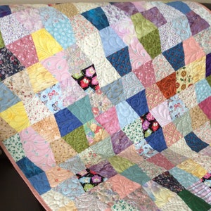 May include: A handmade quilt with a patchwork design. The quilt features a variety of fabrics in shades of pink, blue, green, yellow, and beige. The quilt is quilted with a decorative pattern and has a pink border.
