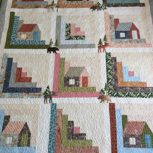 May include: A quilt with a log cabin pattern featuring a variety of fabrics in shades of brown, green, blue, and pink. The quilt is quilted with a swirl pattern and features small images of bears, moose, and trees.
