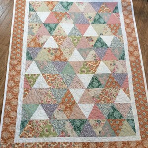 May include: A quilt with a patchwork design featuring a variety of floral patterns in shades of pink, green, brown, and white. The quilt is made up of triangular shapes and is bordered with a brown and white patterned fabric.