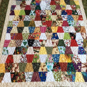 May include: A colorful quilt with a geometric pattern of triangles and diamonds. The quilt is made of various fabrics with Christmas-themed prints. The quilt is edged with a green border.