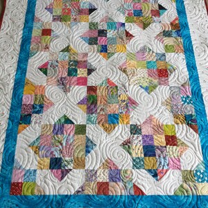 May include: A colorful patchwork quilt with a white background and a blue border. The quilt is quilted with a swirling pattern.