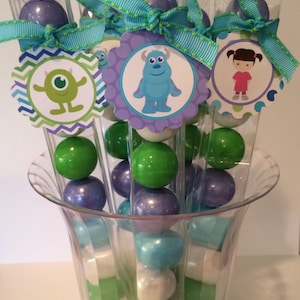 May include: Clear plastic tubes filled with colorful candy balls, decorated with blue, green, and purple monster-themed party favor tags.