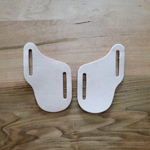 May include: Two white leather pieces with cutouts, resembling a pair of symmetrical shapes.