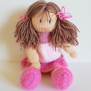 May include: A knitted doll with brown hair, a pink and white striped dress, and pink shoes.