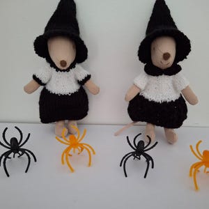 May include: Two plush mouse dolls wearing black knitted witch hats, white knitted tops, and black skirts. The dolls are accompanied by four plastic spider figurines, two of which are black and two of which are orange, arranged in a row.