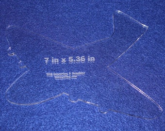 以下が含まれることがあります： 透明なプラスチック製の飛行機ステンシルで、サイズは 17.78 cm × 13.62 cm です。ステンシルは青い表面にあります。