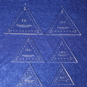 May include: Six clear plastic triangle rulers with different sizes: 2 inches, 1.75 inches, 1.5 inches, 1.25 inches, 1 inch, and .75 inches. Each ruler has a dashed line around the perimeter and three holes.