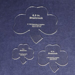 May include: Three clear plastic stencils of shamrocks in different sizes: 6.5 inches, 4 inches, and 3 inches. Each stencil has the text "Shamrock" and the company name and website printed on it.
