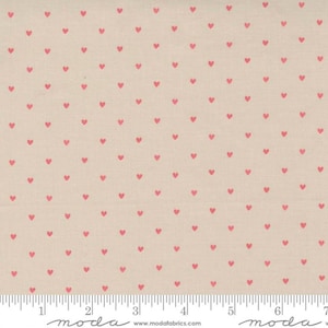 May include: A beige fabric with a repeating pattern of small pink hearts. The fabric is measured in inches with the text "moda" printed on the ruler.