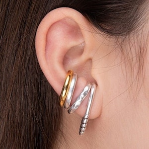 May include: Three ear cuffs in a silver and gold finish. The bottom cuff is a twisted silver design, the middle cuff is a hammered silver design, and the top cuff is a smooth gold band.