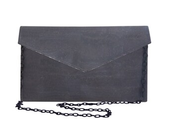 Pode incluir: Uma clutch cinza escuro com uma alça de corrente. A clutch tem um fecho de aba e uma superfície texturizada. A alça de corrente também é cinza escuro. O design geral é minimalista e moderno.