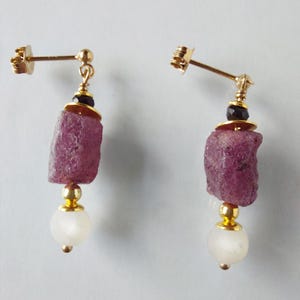 Può includere: Un paio di orecchini d'oro con perline di pietre preziose rosa e bianche. Gli orecchini presentano una perla di pietra preziosa rosa, una perla dorata e una perla di pietra preziosa bianca.