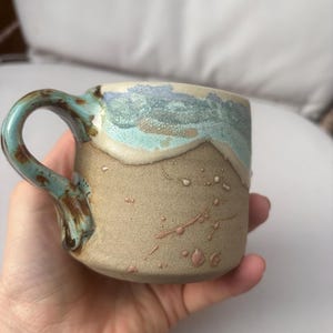 May include: A set of three ceramic mugs with a speckled, matte finish in cream, light grey, and dark grey. Each mug has a simple, minimalist design, ideal for coffee or tea.