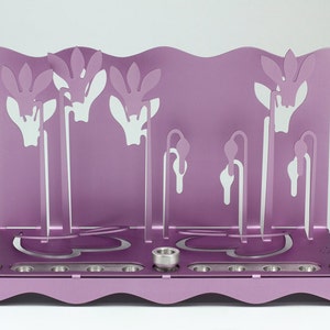 May include: A purple metal menorah with a floral design. The menorah has nine candle holders and a central shamash holder.