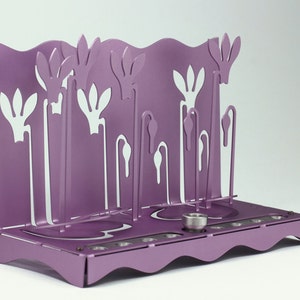 May include: A purple metal menorah with a floral design. The menorah has nine candle holders and a central shamash holder.