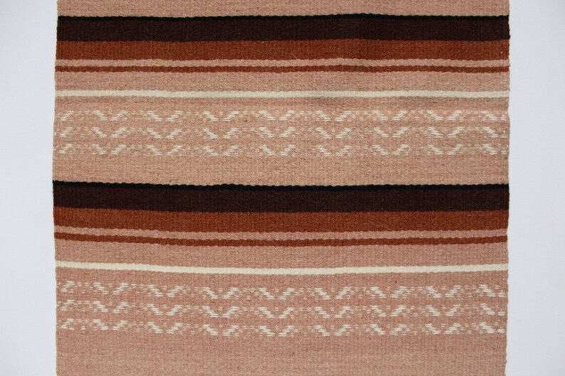 May include: A woven rug with a striped pattern in shades of brown, pink, and white. The rug has a geometric design with a repeating pattern of small triangles.