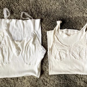 May include: Two white lace-trimmed tank tops. The tank tops are made of a soft, stretchy fabric and have a relaxed fit.