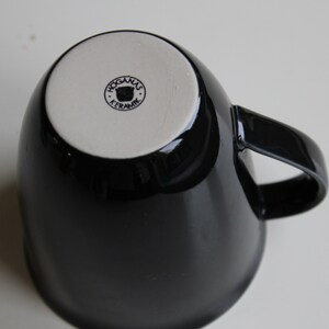 Puede incluir: Taza de cer&aacute;mica negra con fondo blanco y un logotipo que dice "Hogan&auml;s Keramik" con un icono de oso.