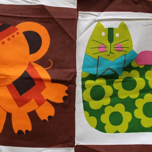 May include: A brown fabric with an orange elephant and a green cat with a blue bow tie. The cat is wearing a green and yellow floral pattern and has a pink and blue striped tail.