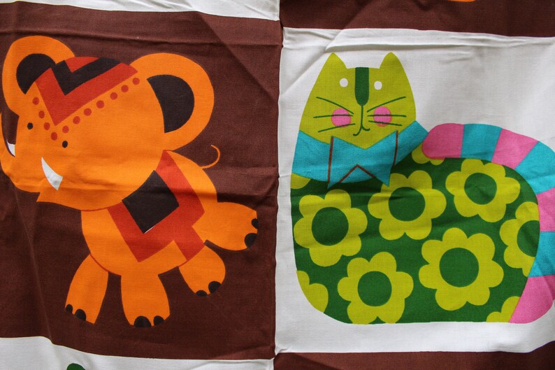 May include: A brown fabric with an orange elephant and a green cat with a blue bow tie. The cat is wearing a green and yellow floral pattern and has a pink and blue striped tail.