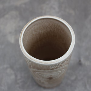 K&ouml;nnte beinhalten: Eine wei&szlig;e Keramikvase mit einem strukturierten, wirbelnden Muster. Die Vase ist leer und hat eine breite &Ouml;ffnung.