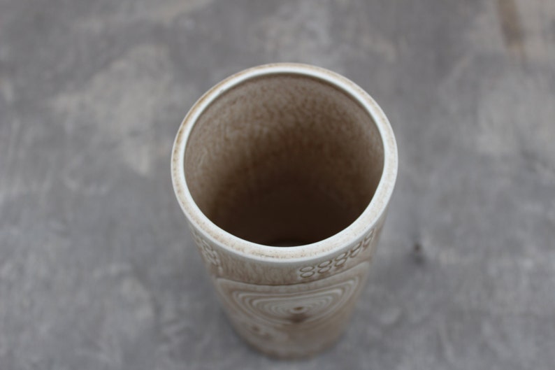 K&ouml;nnte beinhalten: Eine wei&szlig;e Keramikvase mit einem strukturierten, wirbelnden Muster. Die Vase ist leer und hat eine breite &Ouml;ffnung.