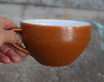 May include: A brown ceramic mug with a white interior. The mug has a rounded shape and a handle.