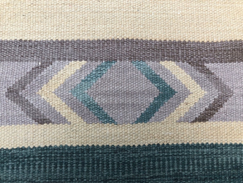 May include: A close-up of a woven rug with a geometric pattern in shades of beige, brown, gray, and teal.