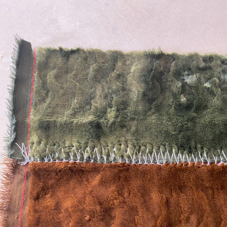 May include: Close-up of a brown and green plush fabric with a white stitched seam. The fabric is soft and fuzzy.