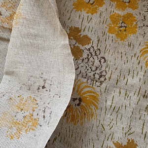 May include: A close-up of a white fabric with a yellow floral pattern. The fabric has a textured, woven look.