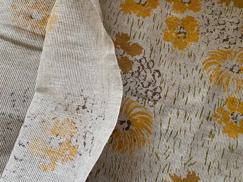 May include: A close-up of a white fabric with a yellow floral pattern. The fabric has a textured, woven look.