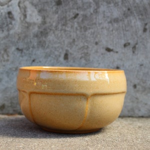 May include: A light brown ceramic bowl with a rounded shape and a slightly textured surface. The bowl has a glossy finish and is perfect for serving or displaying.