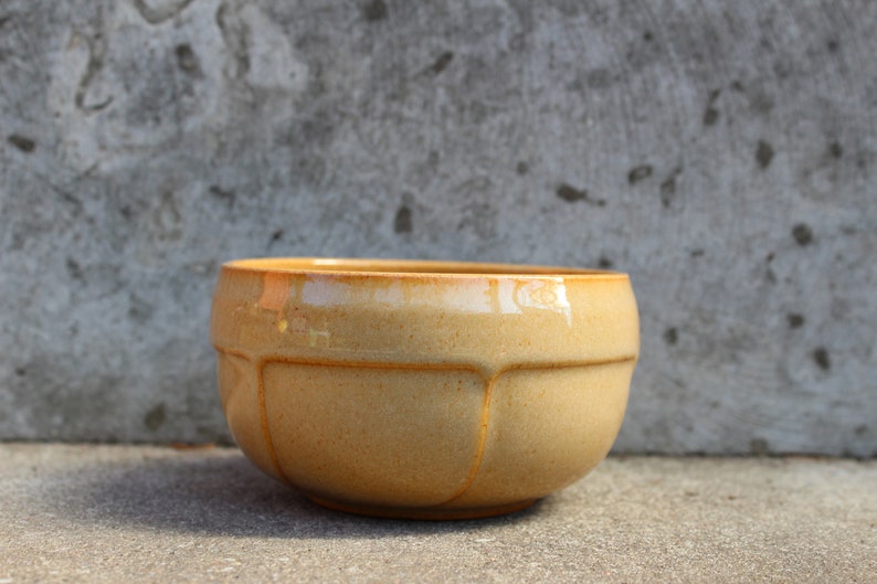 May include: A light brown ceramic bowl with a rounded shape and a slightly textured surface. The bowl has a glossy finish and is perfect for serving or displaying.