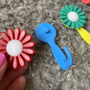 May include: A set of colorful plastic flower-shaped hooks. The hooks are in red, blue, green, and yellow. They are designed to look like daisies with white centers.