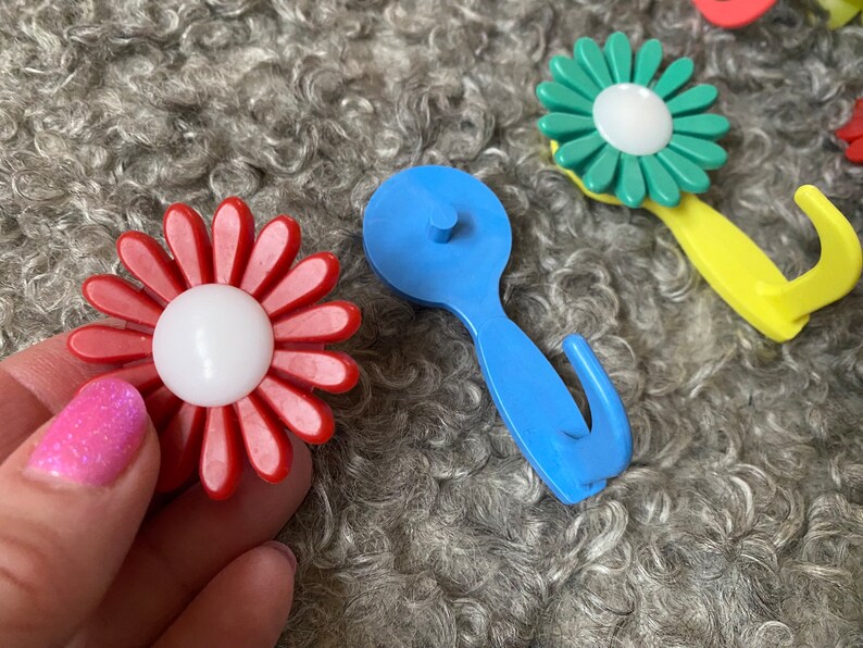 May include: A set of colorful plastic flower-shaped hooks. The hooks are in red, blue, green, and yellow. They are designed to look like daisies with white centers.