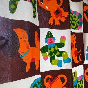 May include: A brown and white fabric with a colorful pattern of animals and a clown. The animals include a dog, a lion, an elephant, a cat, and a bear. The clown is wearing a green and yellow suit with a red hat.