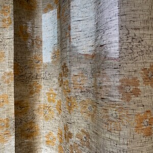 May include: A sheer curtain with a floral pattern in shades of beige and yellow. The curtain is made of a woven fabric with a textured surface.