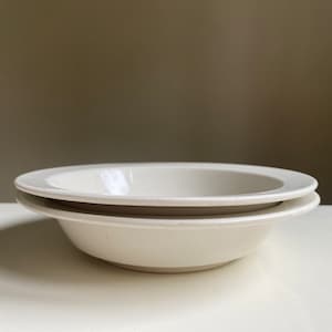 May include: Two white ceramic bowls stacked on top of each other. The bowls are round and have a slight lip around the edge.