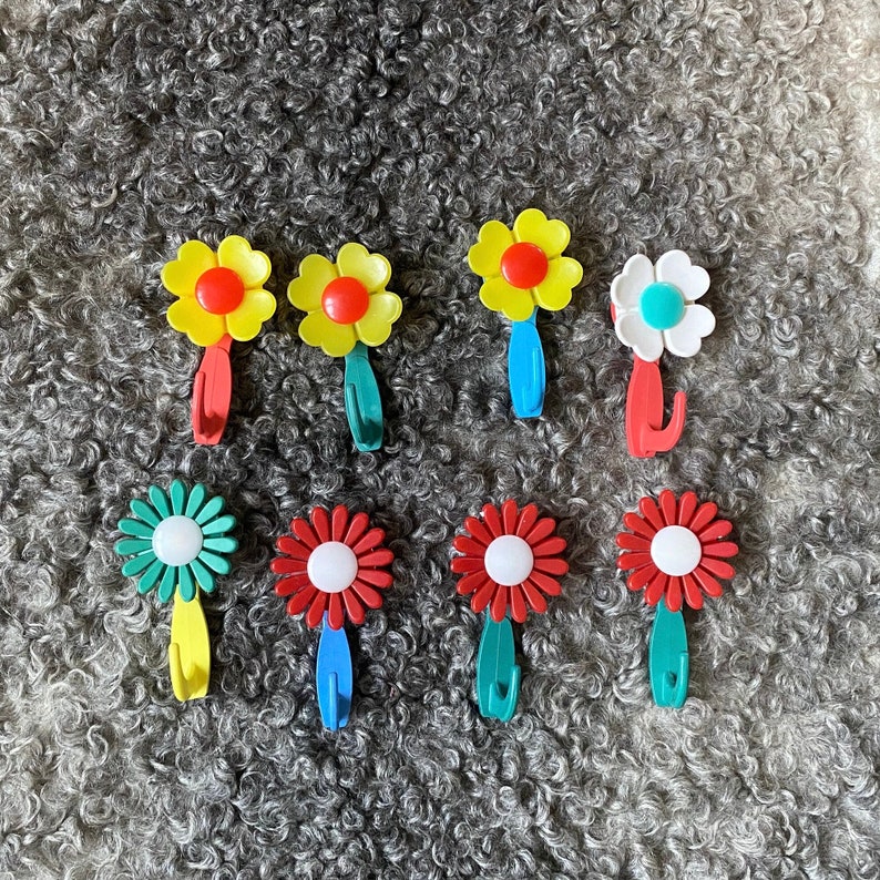 May include: Eight colorful flower-shaped hooks with a yellow, red, and blue color scheme. The hooks are made of plastic and have a whimsical design.