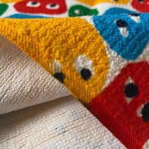 Pu&ograve; includere: Un asciugamano bianco piegato con un motivo colorato di facce di cartoni animati in rosso, giallo, blu e verde. La trama dell'asciugamano &egrave; visibile, con un aspetto morbido e assorbente. Il design &egrave; giocoso e adatto a un bagno o alla spiaggia.