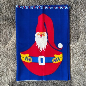 Pode incluir: Um tecido azul com um design de gnomo vermelho e branco. O gnomo está usando um chapéu vermelho e tem uma barba branca. O gnomo está segurando uma bolsa vermelha e branca.