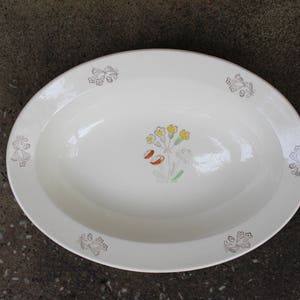 May include: White oval serving dish with a floral design in shades of yellow, green, and orange. The design features a cluster of flowers with five petals each, surrounded by leaves.
