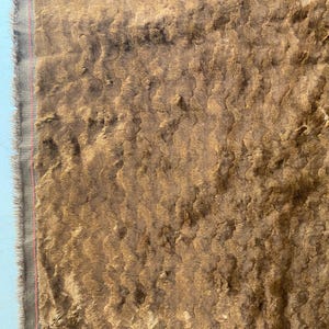 May include: Close-up of a brown faux fur fabric with a textured, wavy pattern. The fabric has a soft, plush feel and is ideal for upholstery or crafting projects.