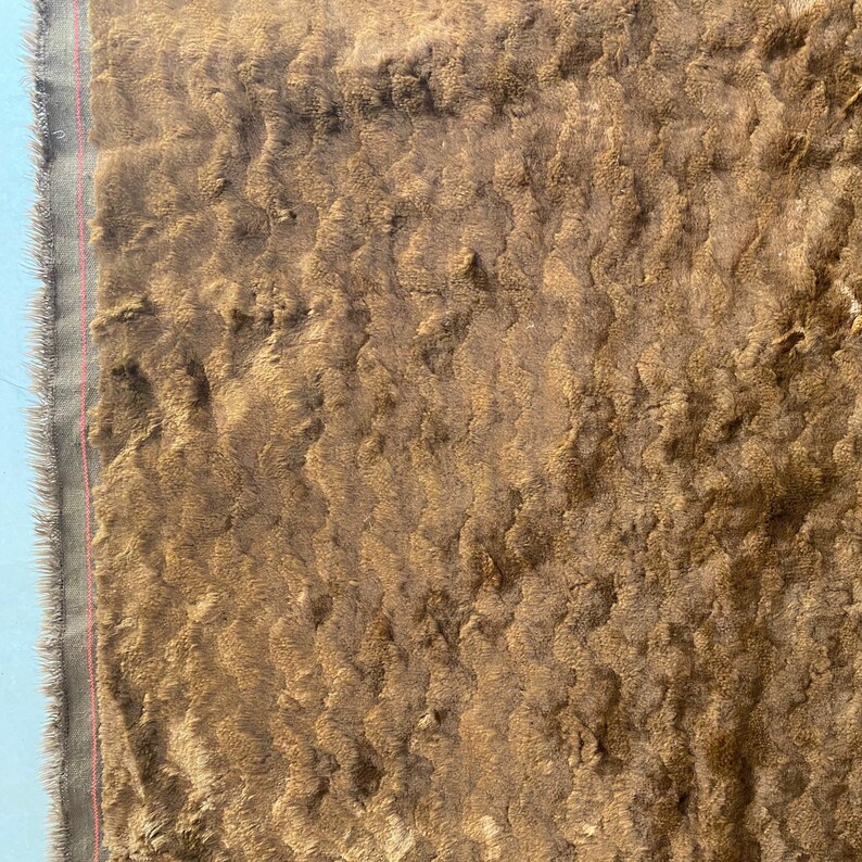 May include: Close-up of a brown faux fur fabric with a textured, wavy pattern. The fabric has a soft, plush feel and is ideal for upholstery or crafting projects.