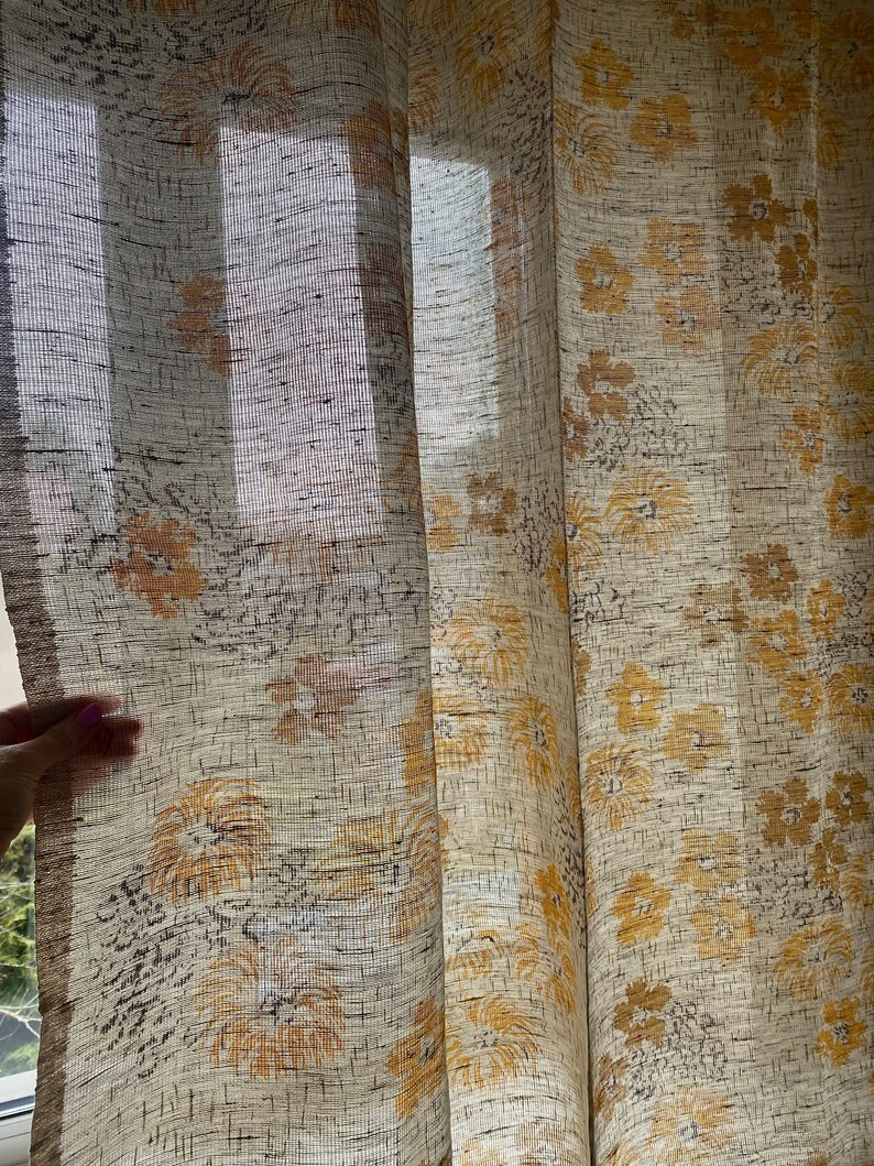May include: A pair of sheer curtains with a floral pattern in shades of beige and yellow. The curtains are made of a lightweight fabric and have a subtle texture.