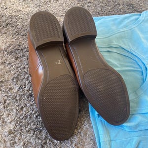 May include: A pair of brown leather shoes with a textured sole. The shoes are on a light brown fuzzy surface and a light blue fabric surface.