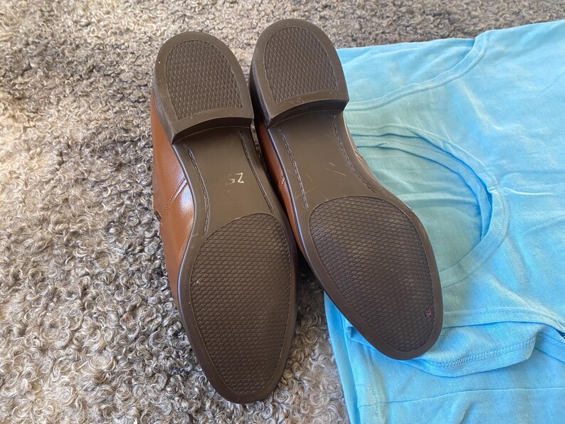 May include: A pair of brown leather shoes with a textured sole. The shoes are on a light brown fuzzy surface and a light blue fabric surface.
