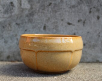 May include: A light brown ceramic bowl with a rounded shape and a slightly textured surface.