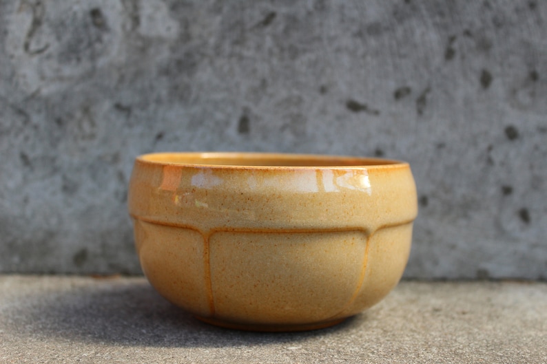 May include: A light brown ceramic bowl with a rounded shape and a slightly textured surface.