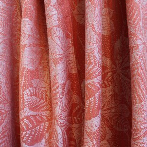 May include: A close-up of a coral-colored fabric with a white floral pattern. The fabric has a soft, textured feel and is perfect for curtains, upholstery, or clothing.